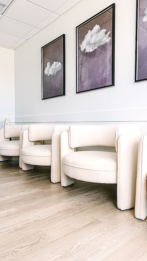 In BeSpoke Orthodontics in Burtonsville, MD, modern cream chairs sit below cloud art in a minimalist room with light wood floors.