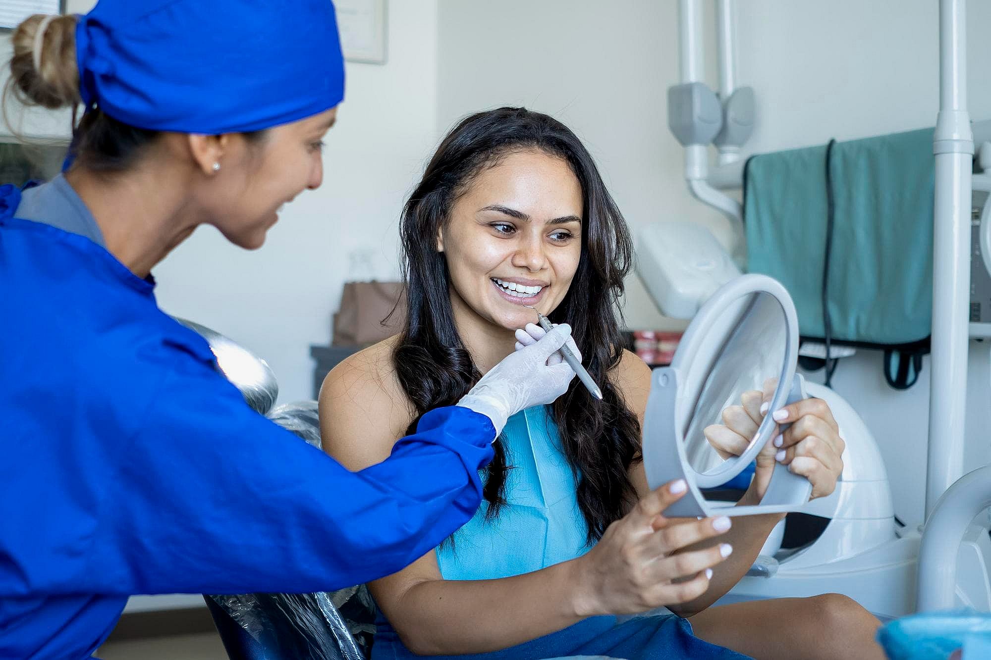 At BeSpoke Orthodontics in Burtonsville, MD, a dental professional in blue scrubs shows a patient her teeth in a hand mirror for new Palatal Expander.