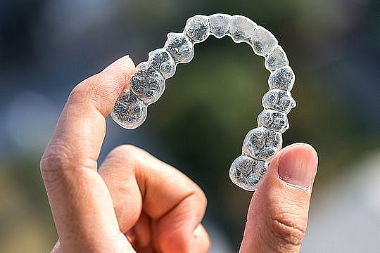 A hand holds a Invisalign clear dental aligner with a blurred background, showcasing BeSpoke Orthodontics in Burtonsville, MD.