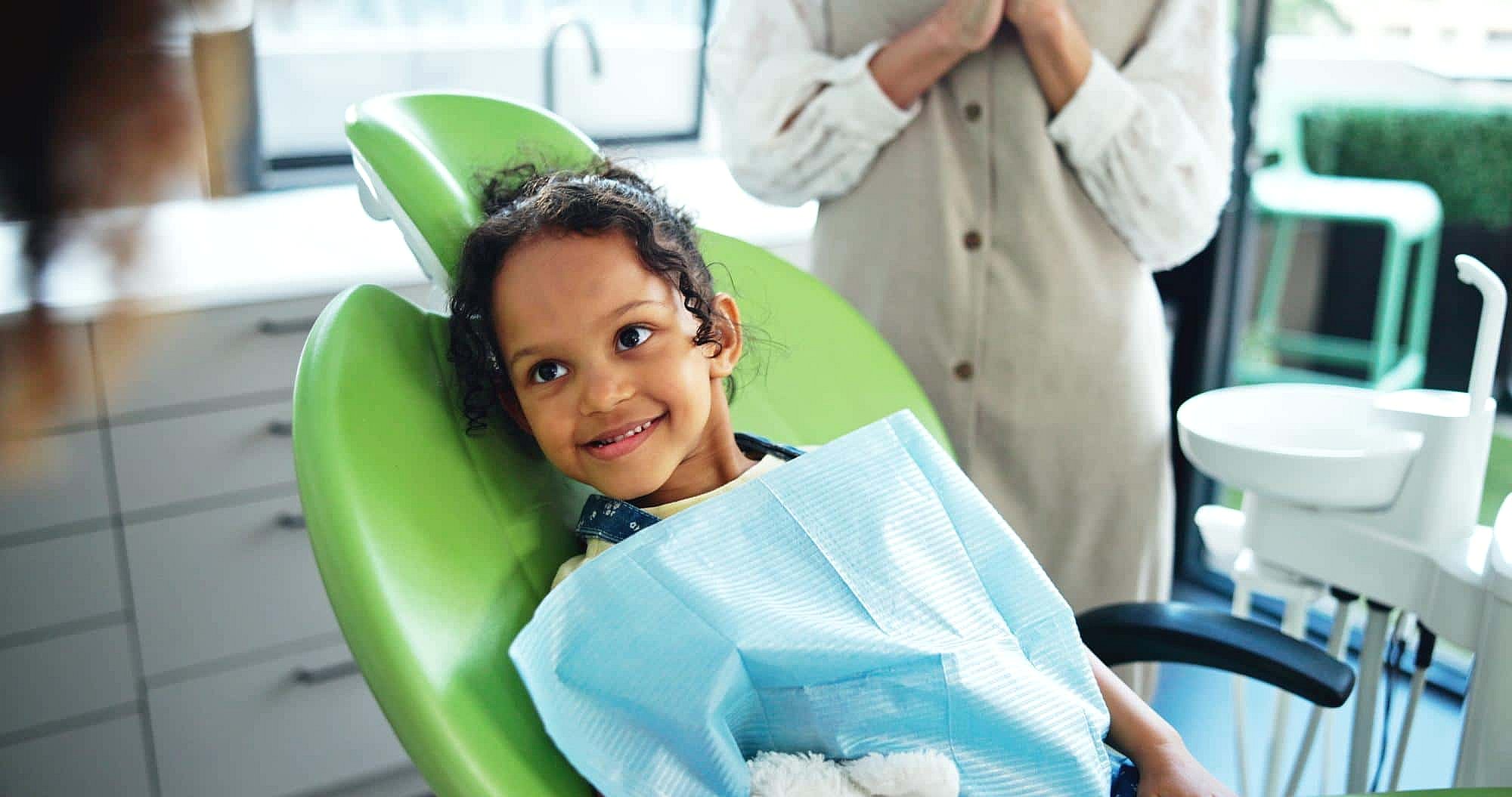 At BeSpoke Orthodontics in Burtonsville, MD, a smiling child with a blue bib holds a stuffed animal in a green dental chair.
