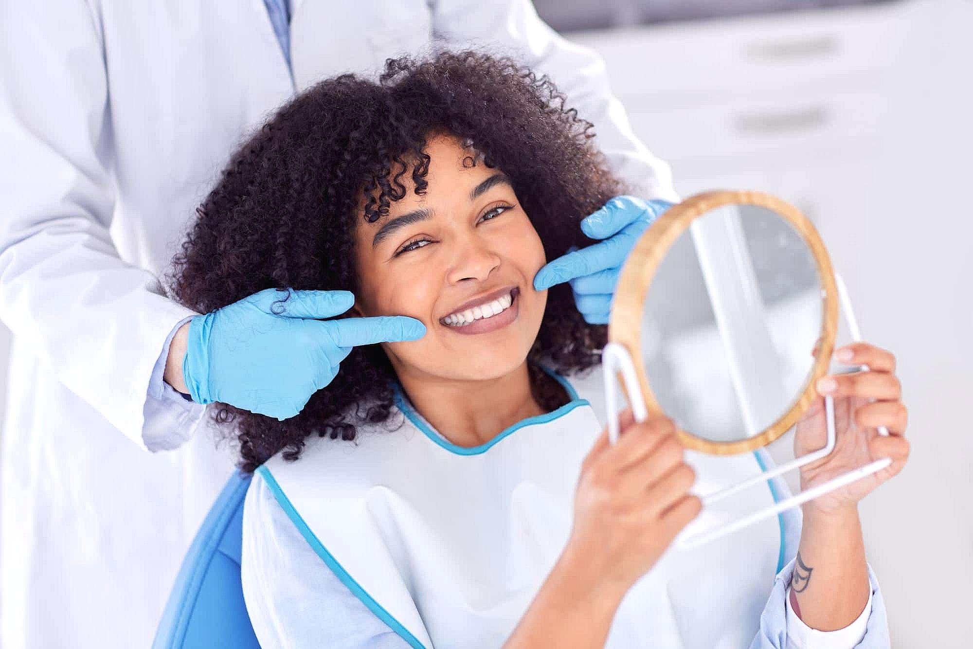 A dentist in gloves discusses orthodontic appliances at BeSpoke Orthodontics in Burtonsville, MD, with a smiling patient holding a mirror.