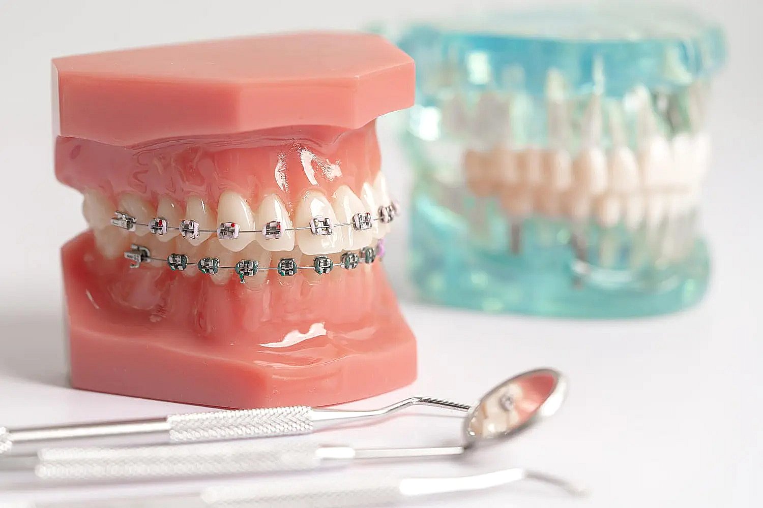 Dental models with and without metal braces are shown with tools at BeSpoke Orthodontics in Burtonsville, MD, on a white surface.