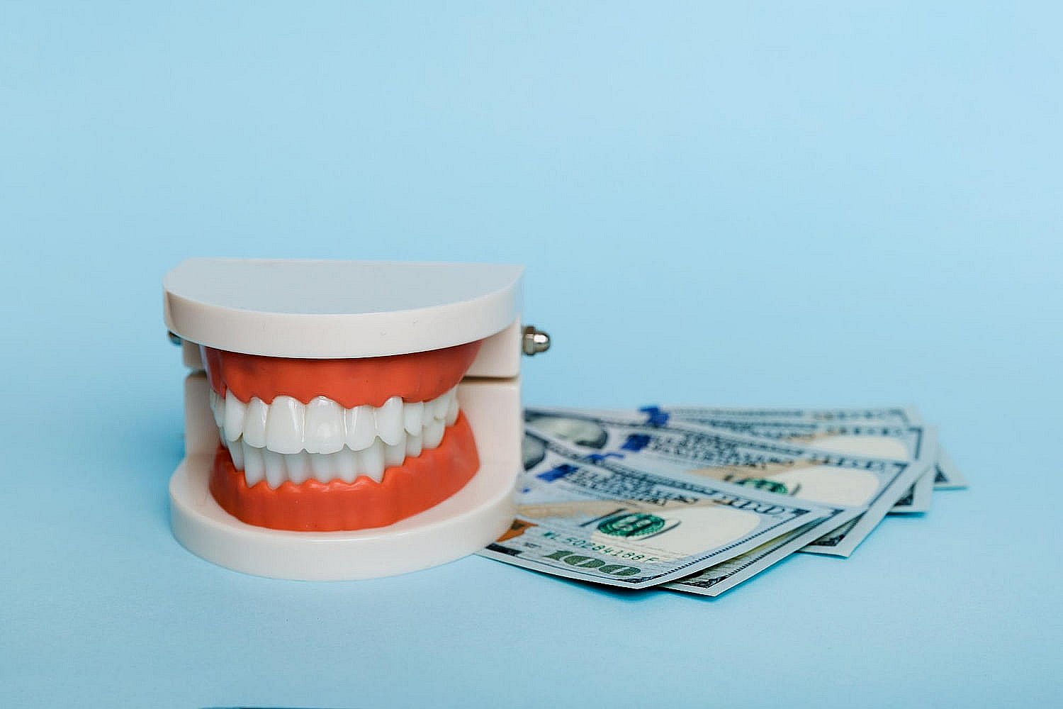 Artificial teeth model beside hundred-dollar bills, representing the cost of clear braces at BeSpoke Orthodontics in Burtonsville, MD, on blue background.