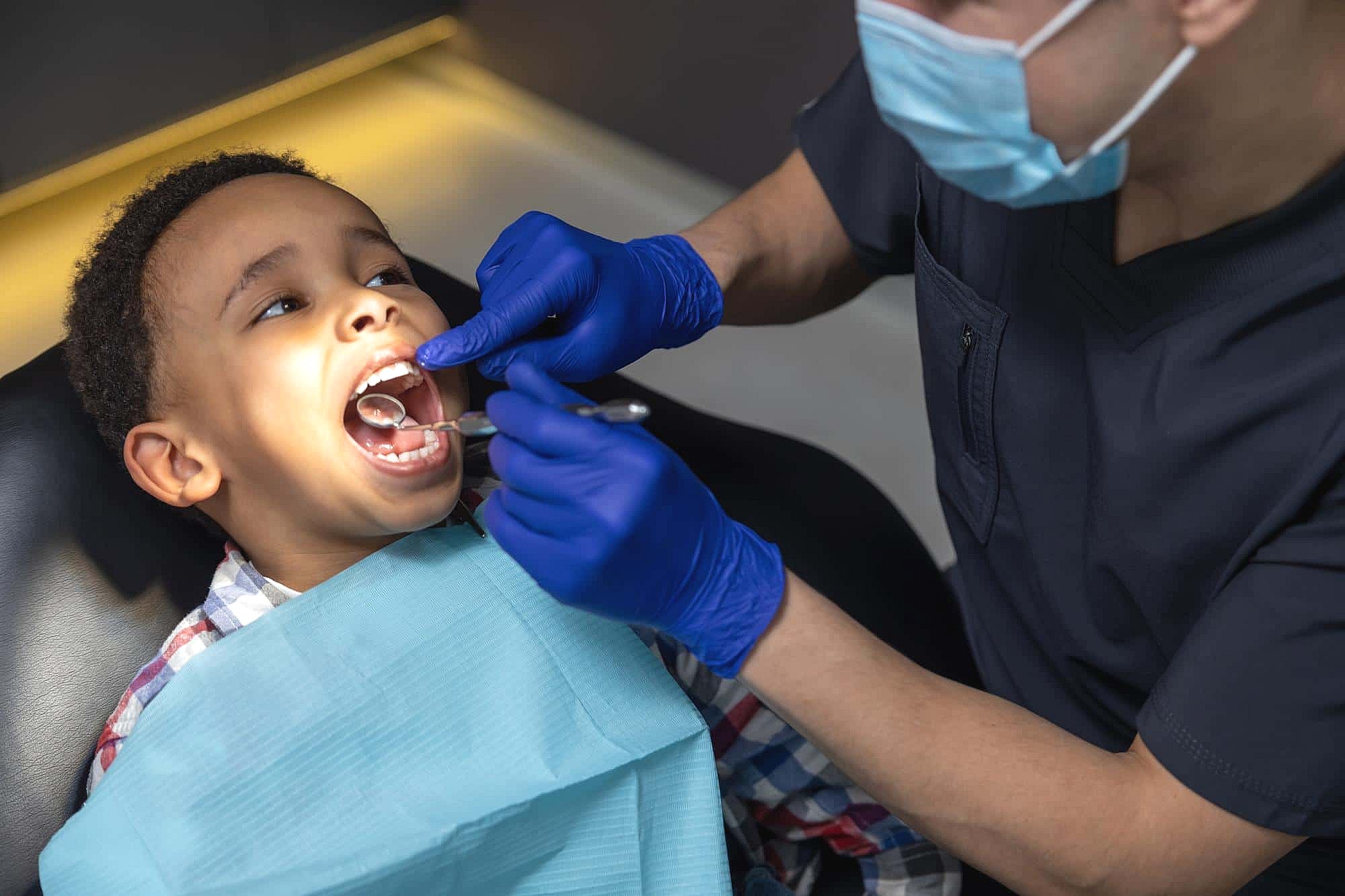 At BeSpoke Orthodontics in Burtonsville, MD, a child gets a dental checkup from a masked orthodontist using dental tools.