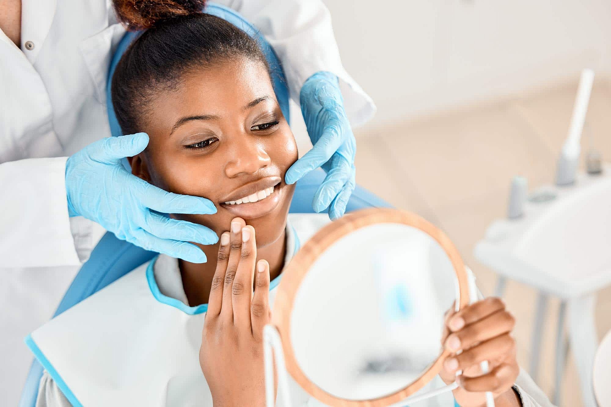 At BeSpoke Orthodontics in Burtonsville, MD, a woman smiles in a dental chair as a dentist examines her face for an orthodontic appliance.