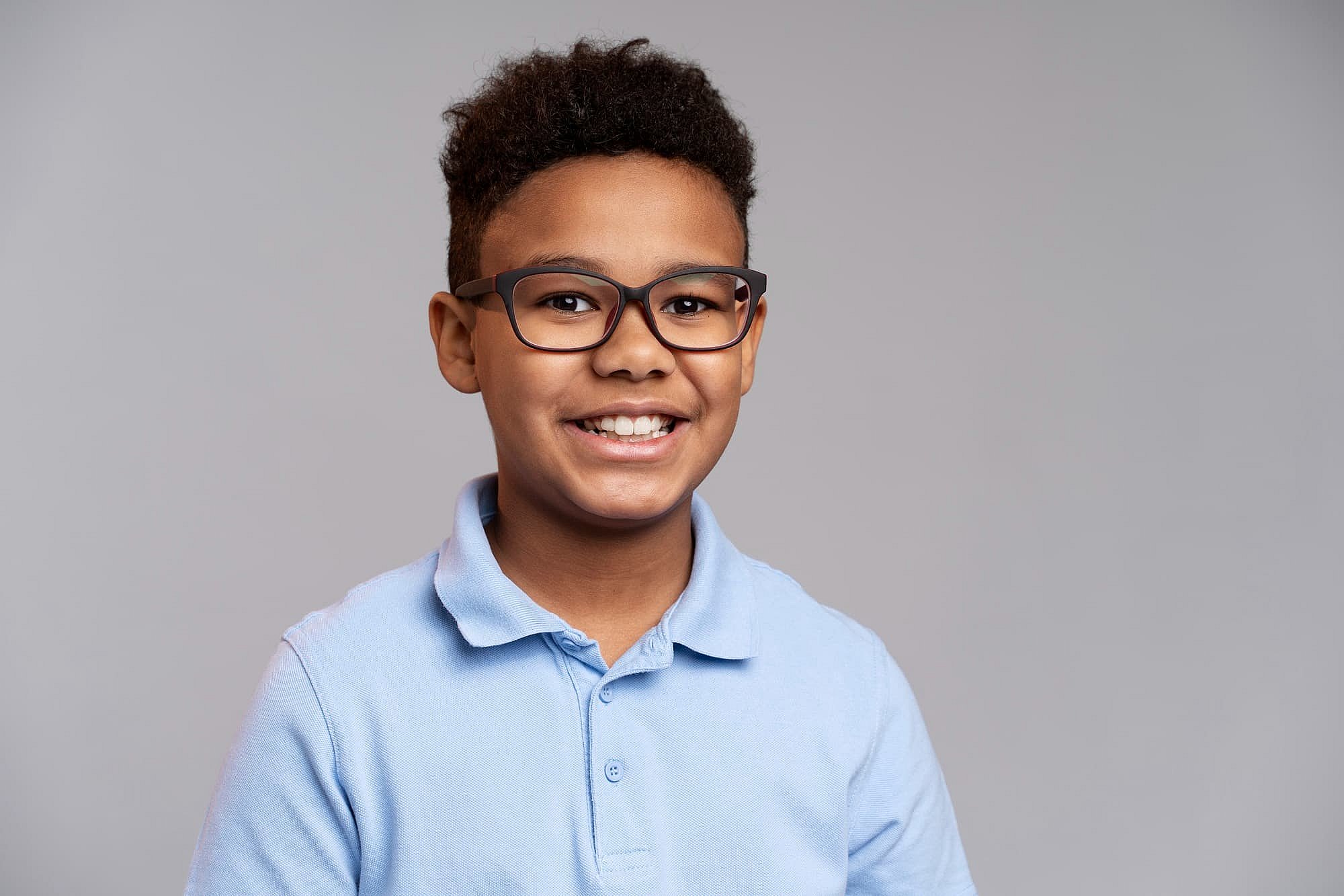 Confident, smiling boy with short curly hair and glasses in a blue polo, perfect for BeSpoke Orthodontics in Burtonsville, MD.