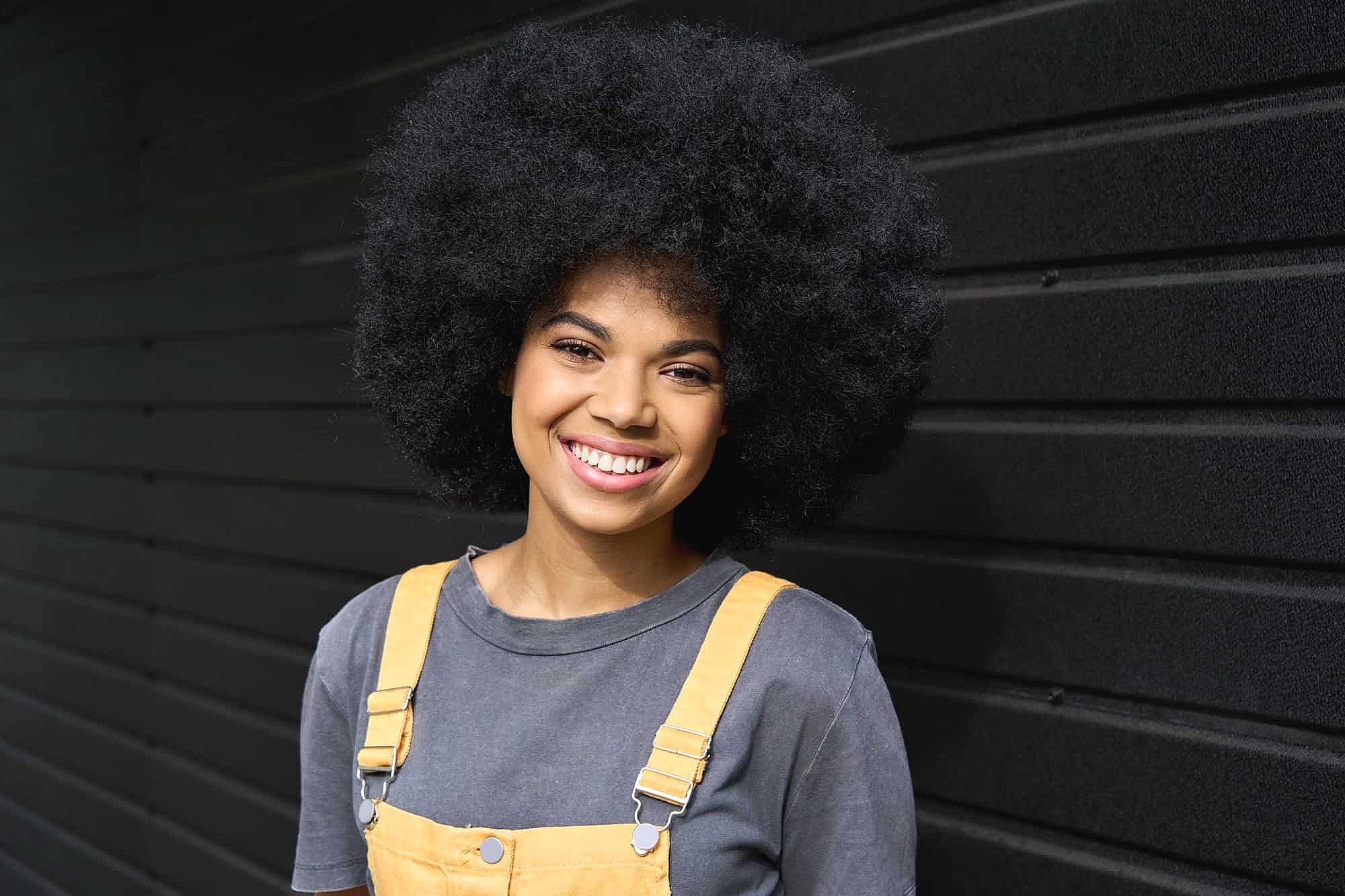 Smiling in front of a black metal wall, a young woman shows her braces from BeSpoke Orthodontics in Burtonsville, MD.