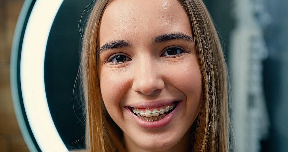 Bespoke Orthodontics Smiling with clear braces, a young person at BeSpoke Orthodontics in Burtonsville, MD; circular light glows in the background.