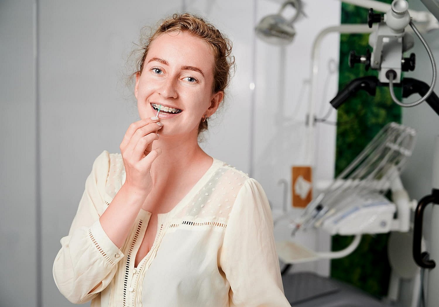 Smiling young woman with ceramic braces inserts a dental aligner at BeSpoke Orthodontics in Burtonsville, MD, clinic equipment behind her.