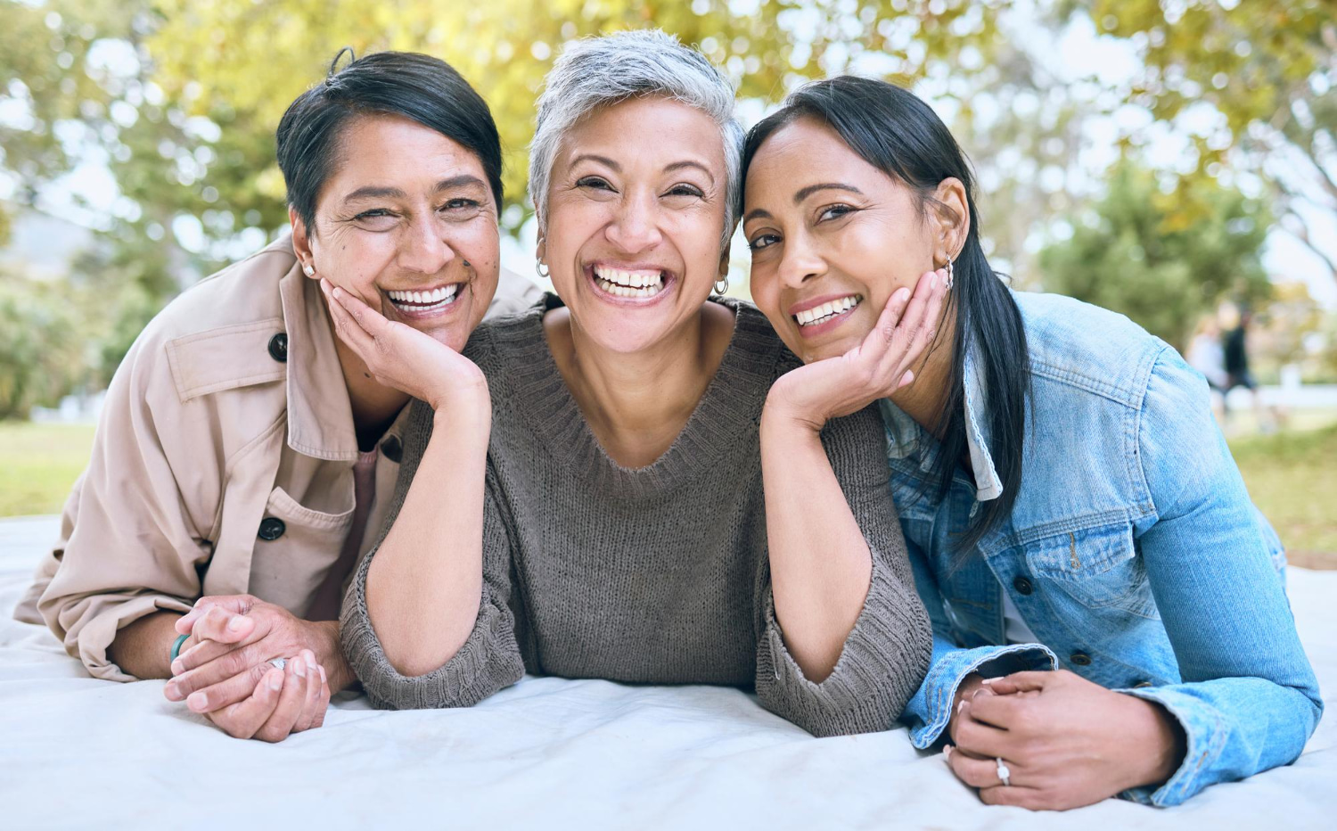 Enjoying the outdoors in Burtonsville, MD, three women relax smiling, choosing the right Adult Orthodontics at BeSpoke Orthodontics among green trees.