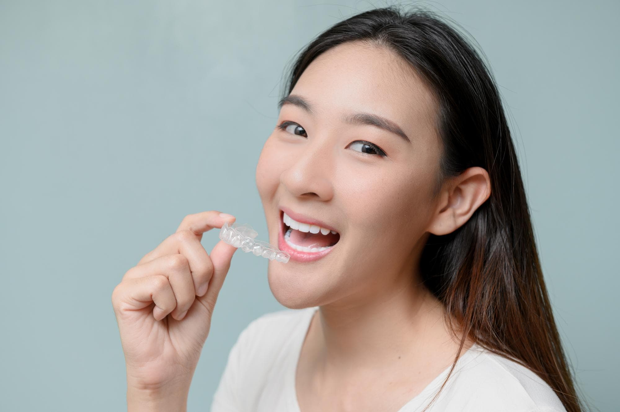 Smiling, a woman holds a Invisalign® Clear Aligners near her open mouth; BeSpoke Orthodontics in Burtonsville, MD.