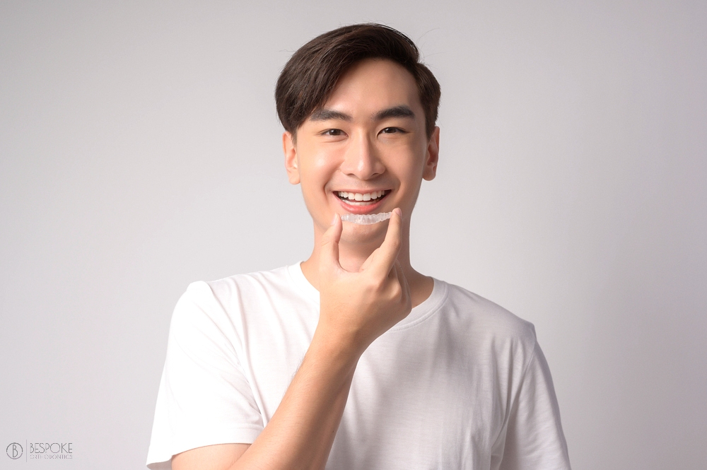 young smiling man holding invisalign clear aligners white - Can Invisalign Fix Overbite in Burtonsville, MD 