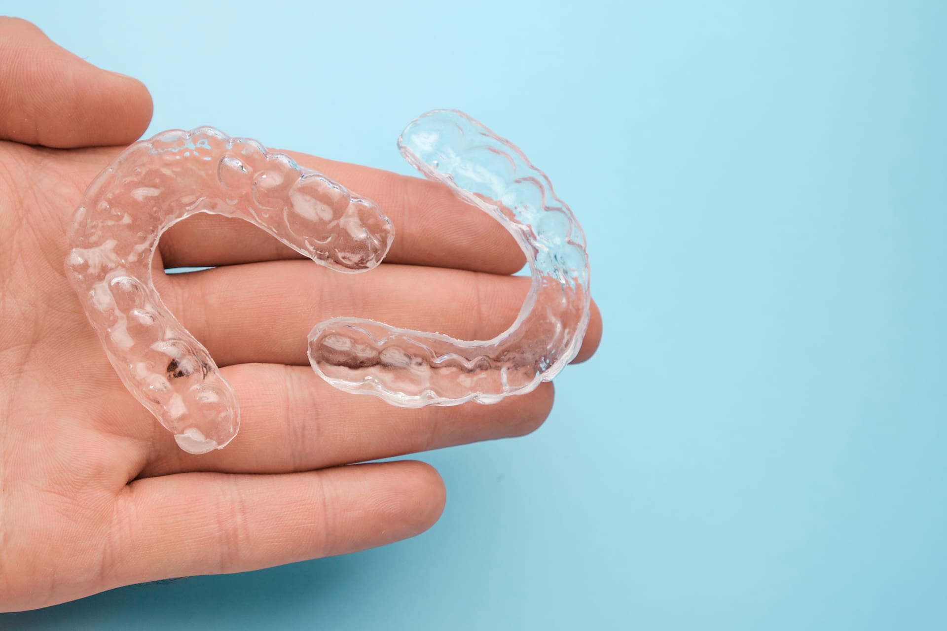 Clear dental aligners held in a hand against a blue background, showcasing BeSpoke Orthodontics’ Invisalign Payment Plan in Burtonsville, MD.