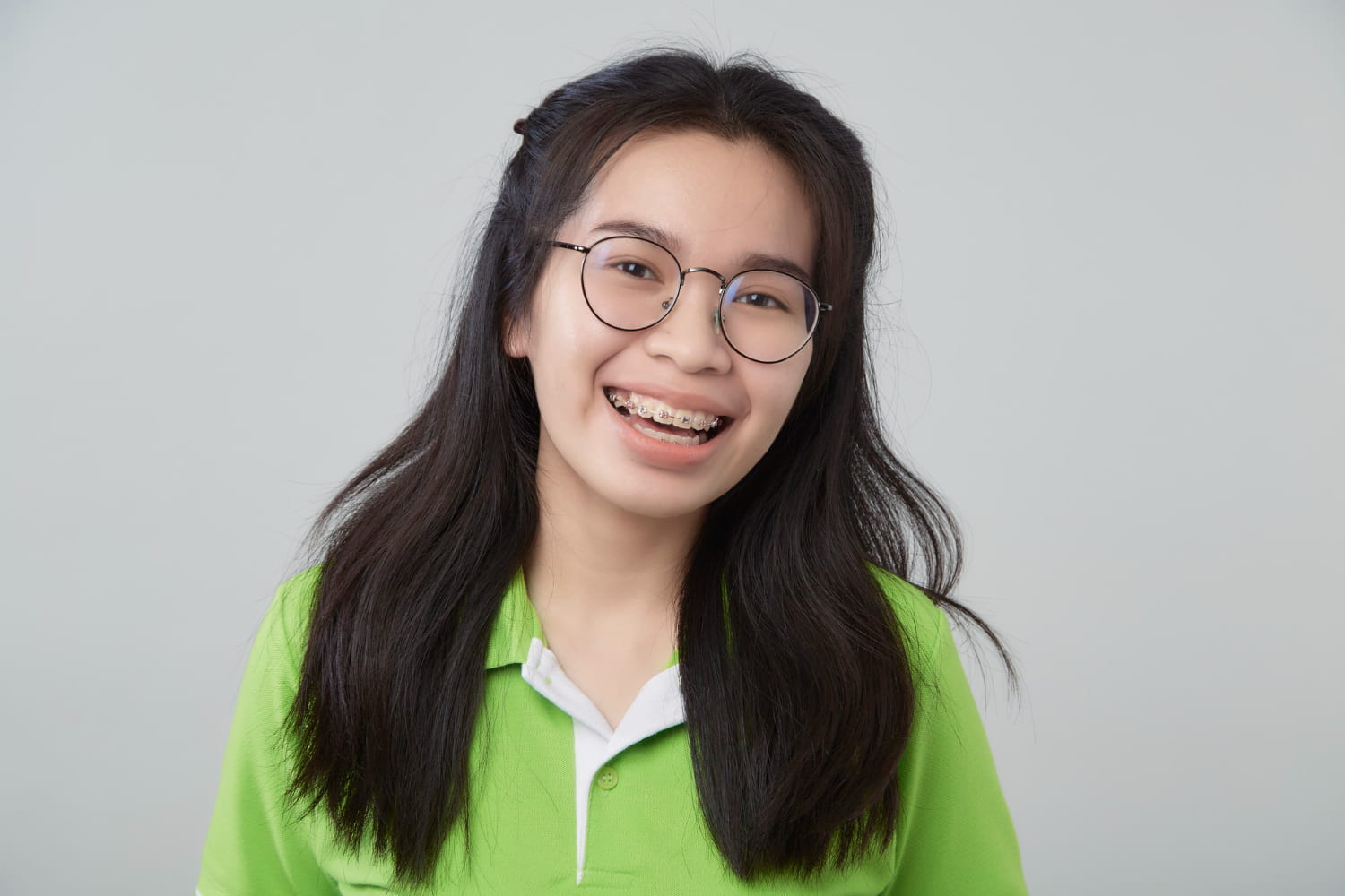 Bespoke Orthodontics Smiling young person with braces wearing glasses and a green shirt, representing BeSpoke Orthodontics in Burtonsville, MD, with focus on braces cost.