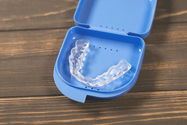A clear dental night guard in a blue case on wood, like those from BeSpoke Orthodontics in Burtonsville, MD for Invisalign payment plans.