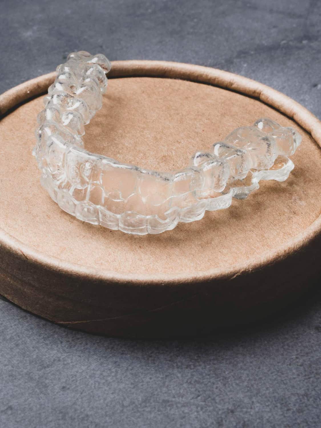 A clear dental aligner on a brown container highlights BeSpoke Orthodontics' Invisalign Payment Plan in Burtonsville, MD.