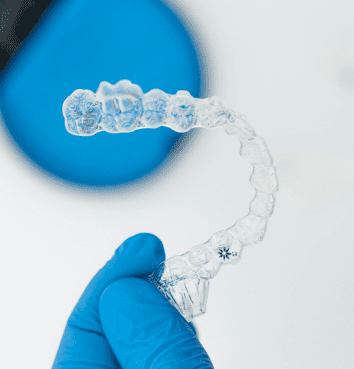 A gloved hand at BeSpoke Orthodontics in Burtonsville, MD holds a clear aligner, promoting Invisalign Payment Plan benefits.