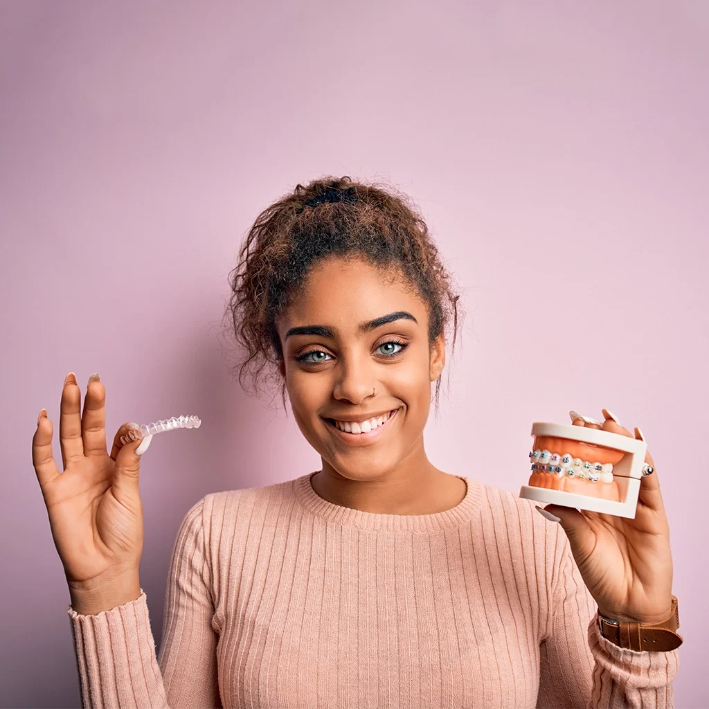 young woman smiling holding metal braces and removable invisible aligner